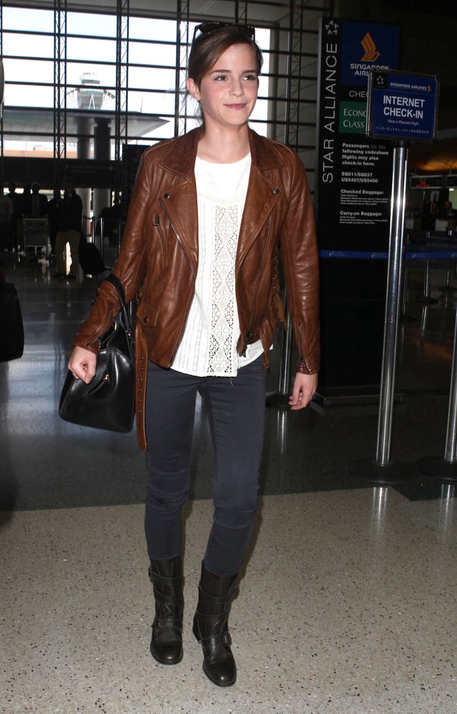 Emma Watson added edgy polish to her airport ensemble with the help of a brown motorcycle jacket and AG velvet jeans.