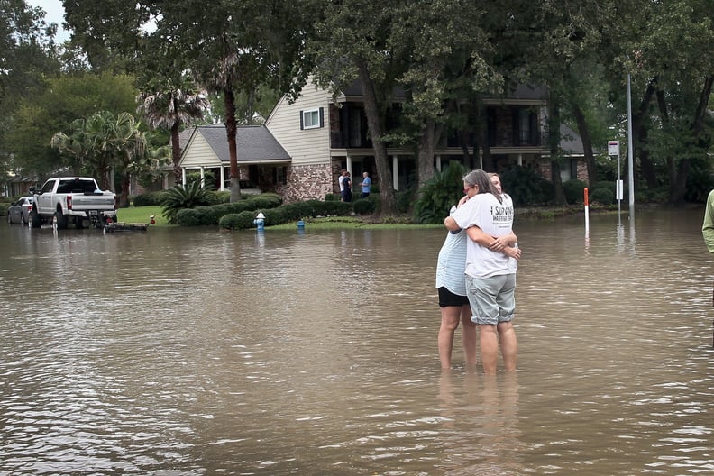 Two people hug on a flooded street in Houston, TX.
