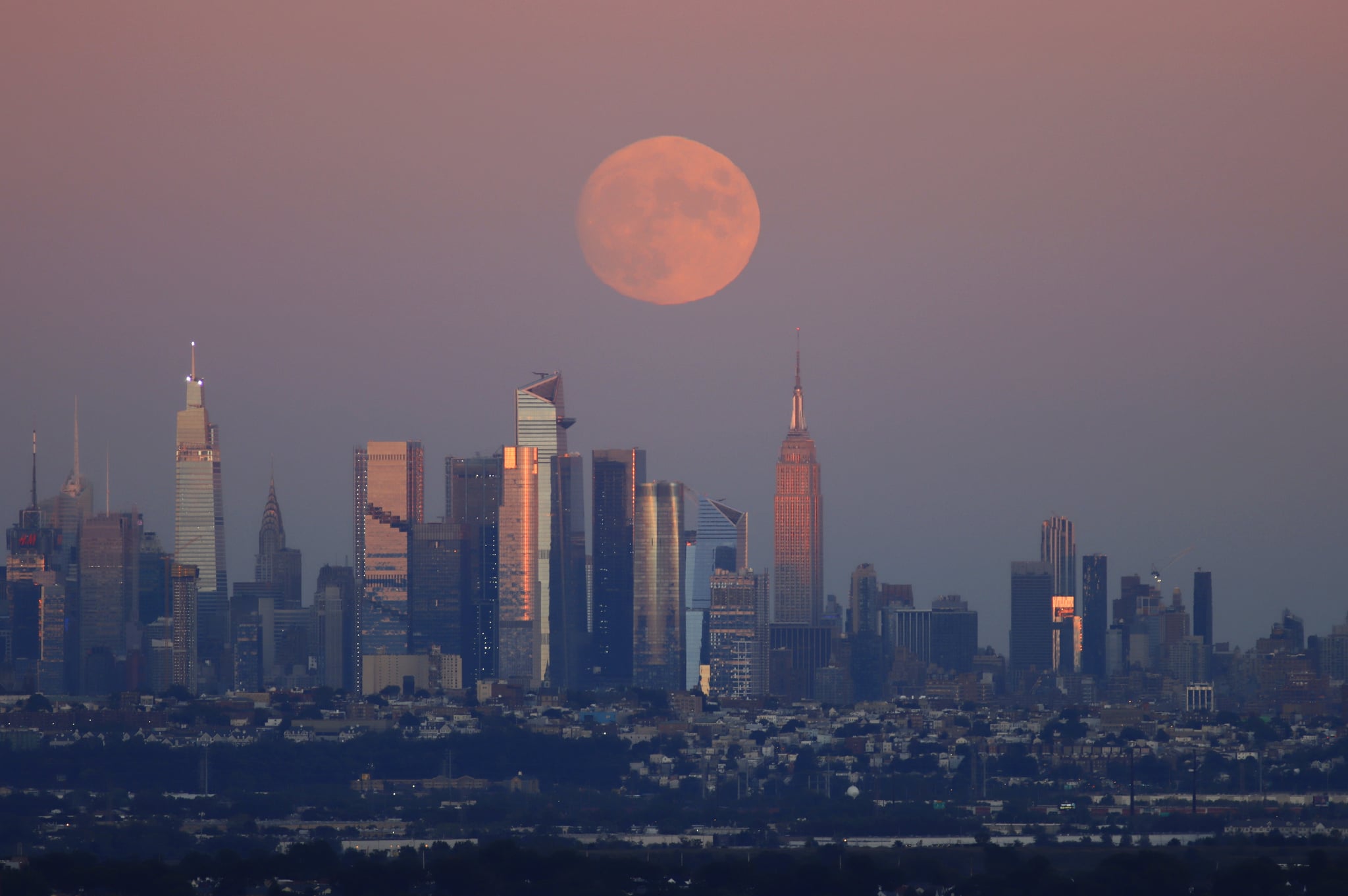 WEST ORANGE, NJ - SEPTEMBER 19: A 98.8 percent Harvest Moon rises behind midtown Manhattan, One Vanderbilt, the Chrysler Building, the Spiral, Hudson Yards and the Empire State Building as the sun sets in New York City on September 19, 2021 as seen from West Orange, New Jersey.  (Photo by Gary Hershorn/Getty Images)