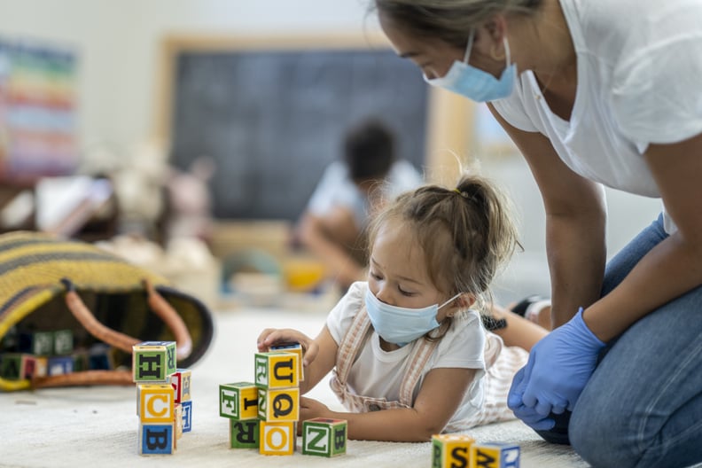 3 year old girl playing at daycare while wearing a protective face mask to protect from the transfer of germs during phase 2 of reopening during COVID-19.