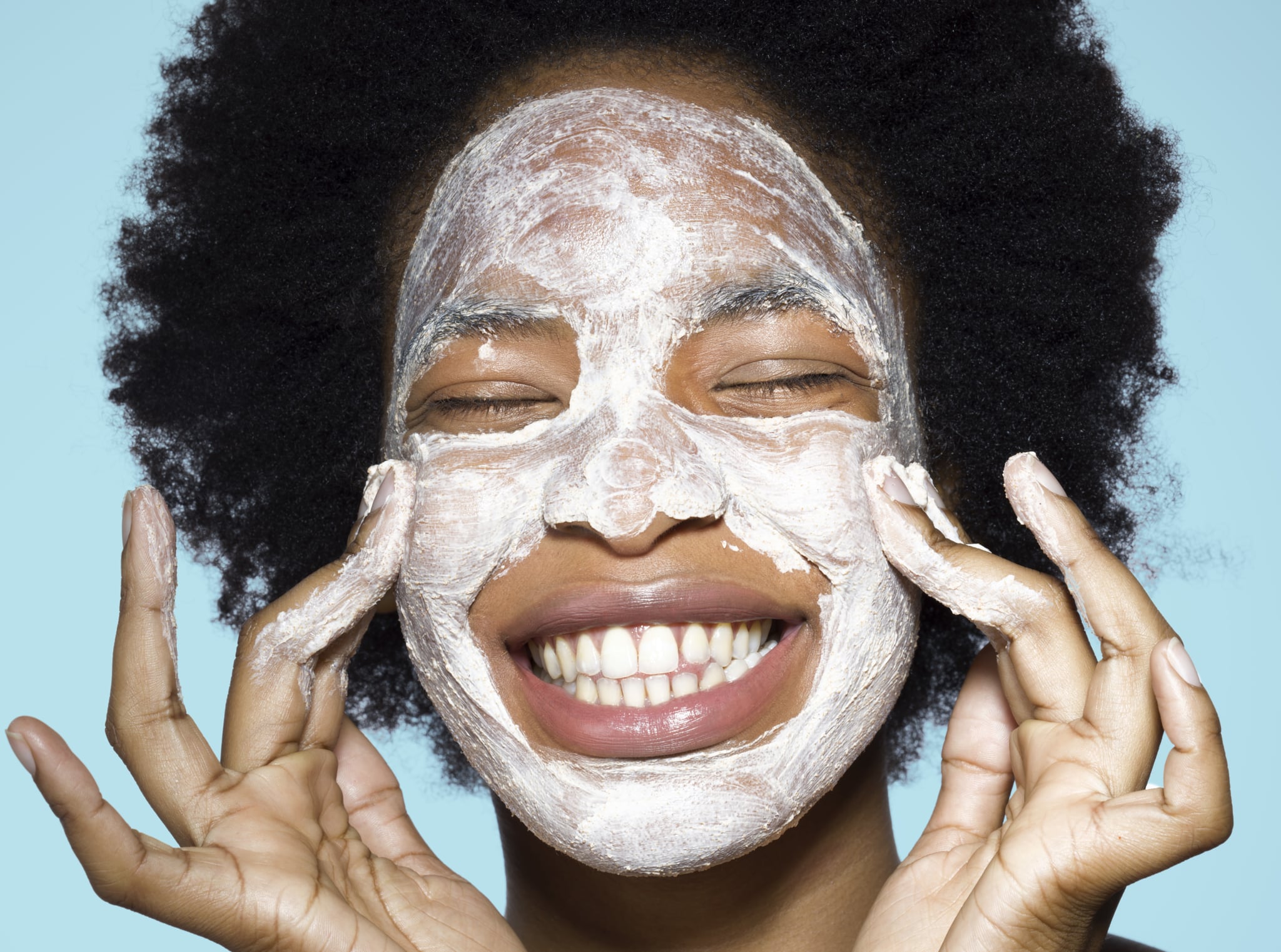 Close-up of young mixed-race woman applying white face cream face, face mask, with turquoise background