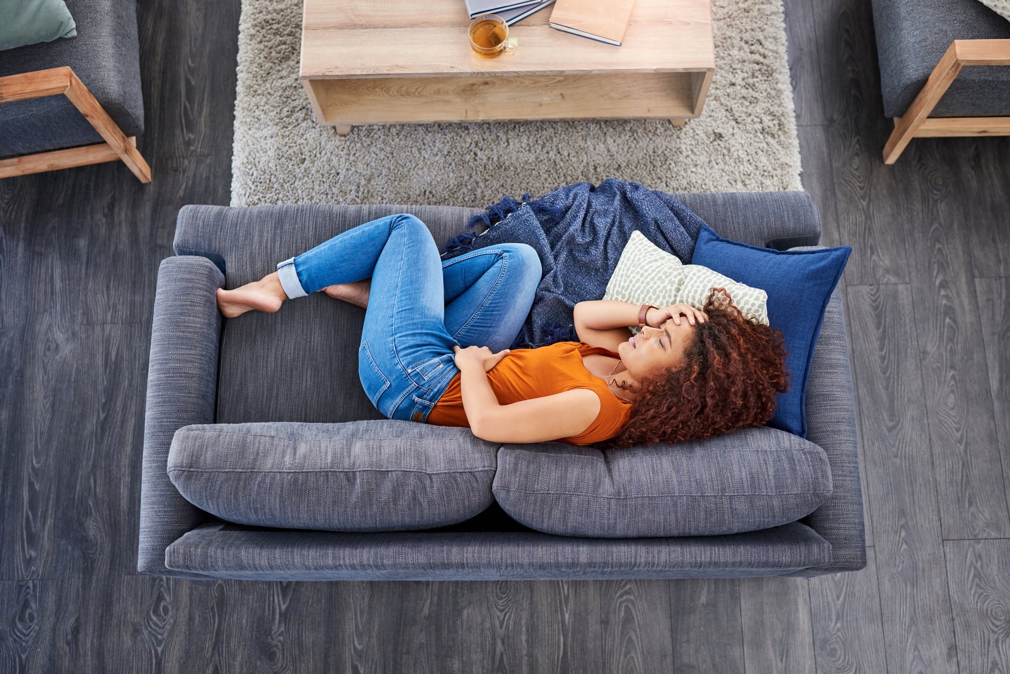 Shot of a young woman suffering from stomach cramps on the sofa at home