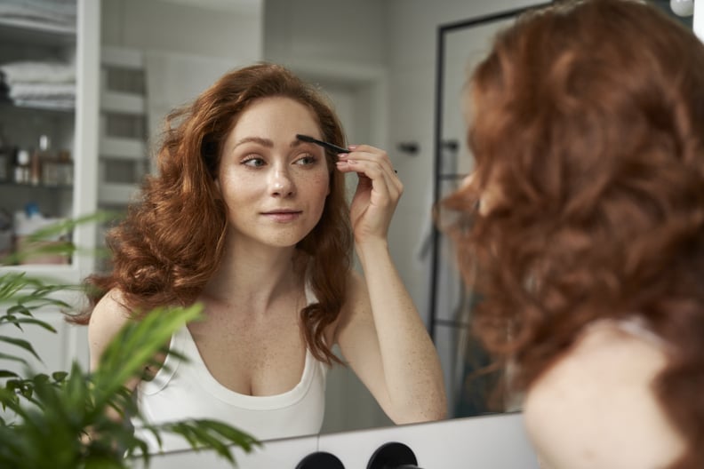Caucasian woman brushing eyebrows in the mirror reflection