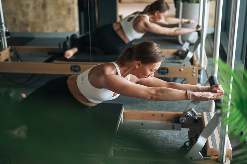 Young woman in sportswear doing Pilates on reformer in modern studio.