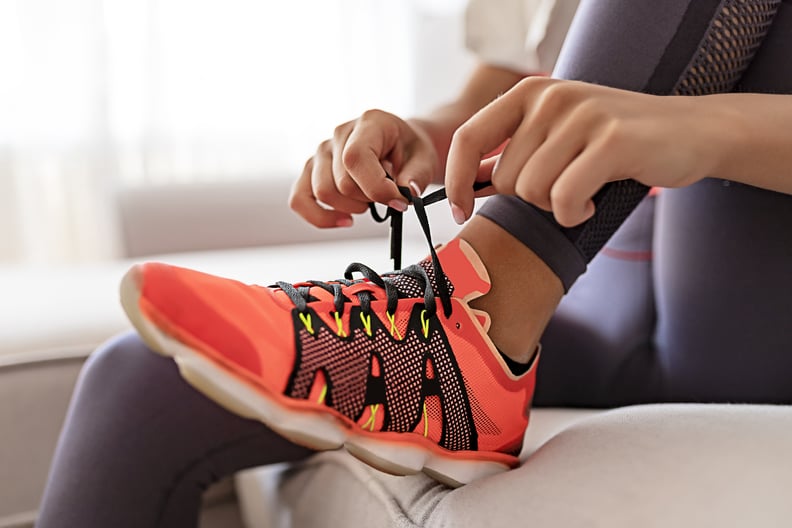 Young Woman Sitting in Living Room and Tying Shoelaces on Sneakers and Getting Ready for Fitness. Healthy Lifestyle Concept