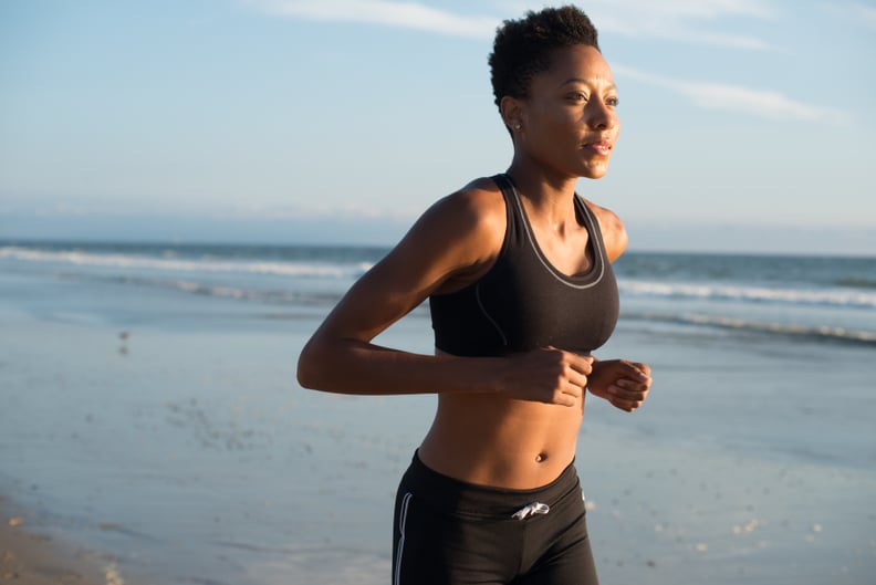 Black woman runs along the beach by the ocean