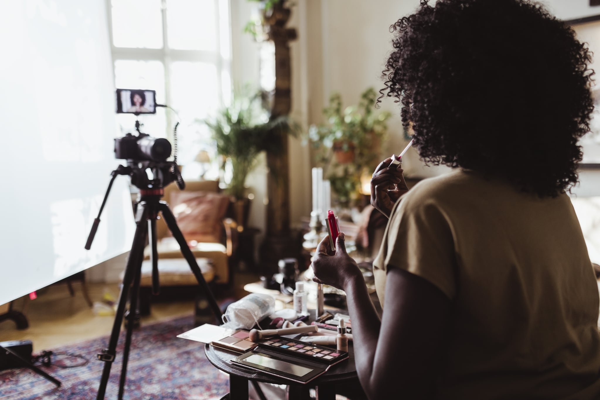 A photo shows a Black beauty content creator making a video with lip gloss.