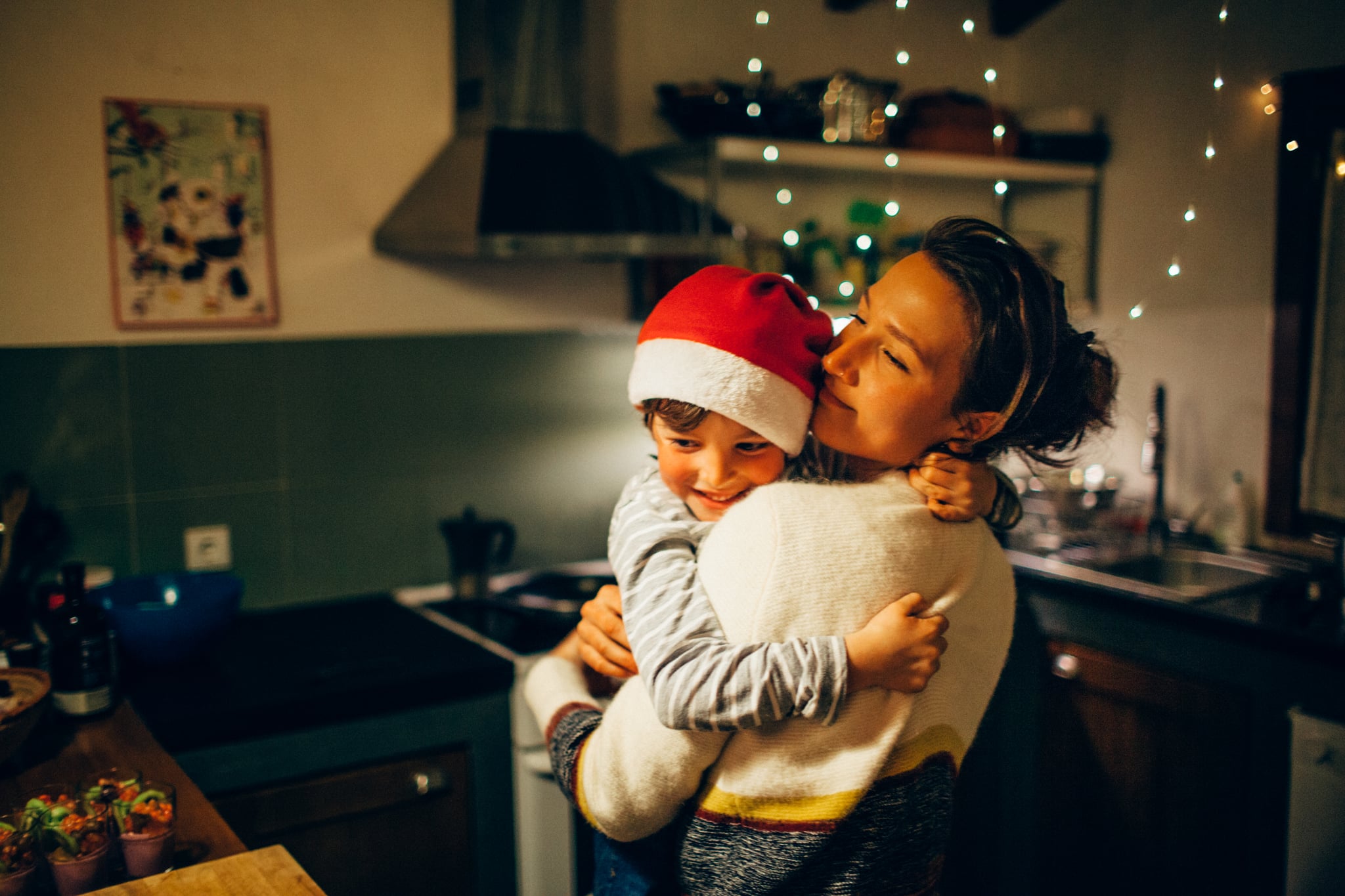 mom hugging her son wearing a Santa hat in the kitchen