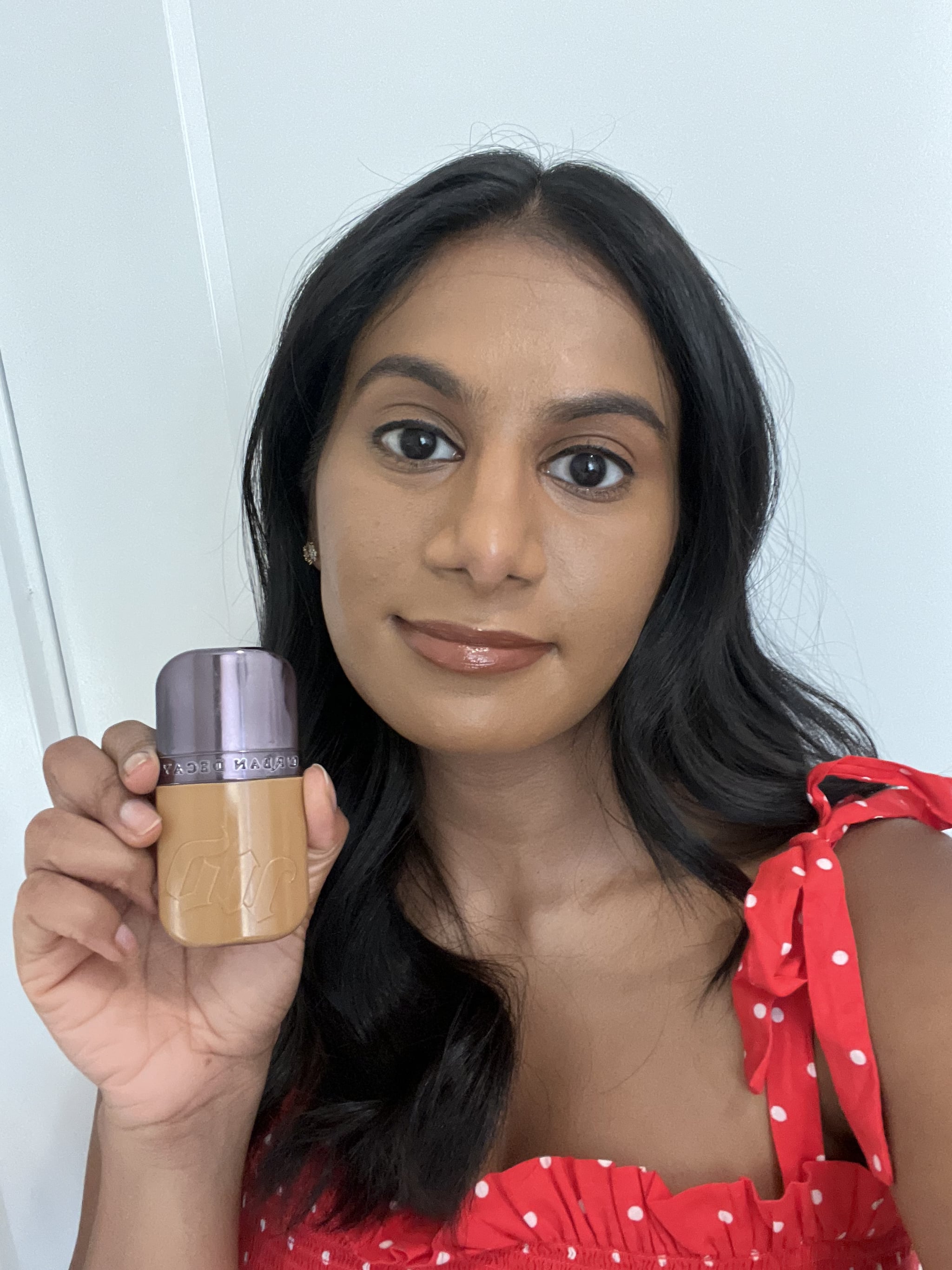 Woman wearing and holding the Urban Decay Face Bond Foundation.