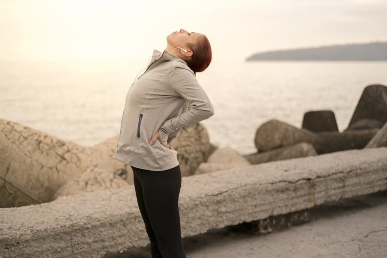 Photo taken on sunset in Bulgaria, Eastern Europe. Sporty young woman having back pains during workout.