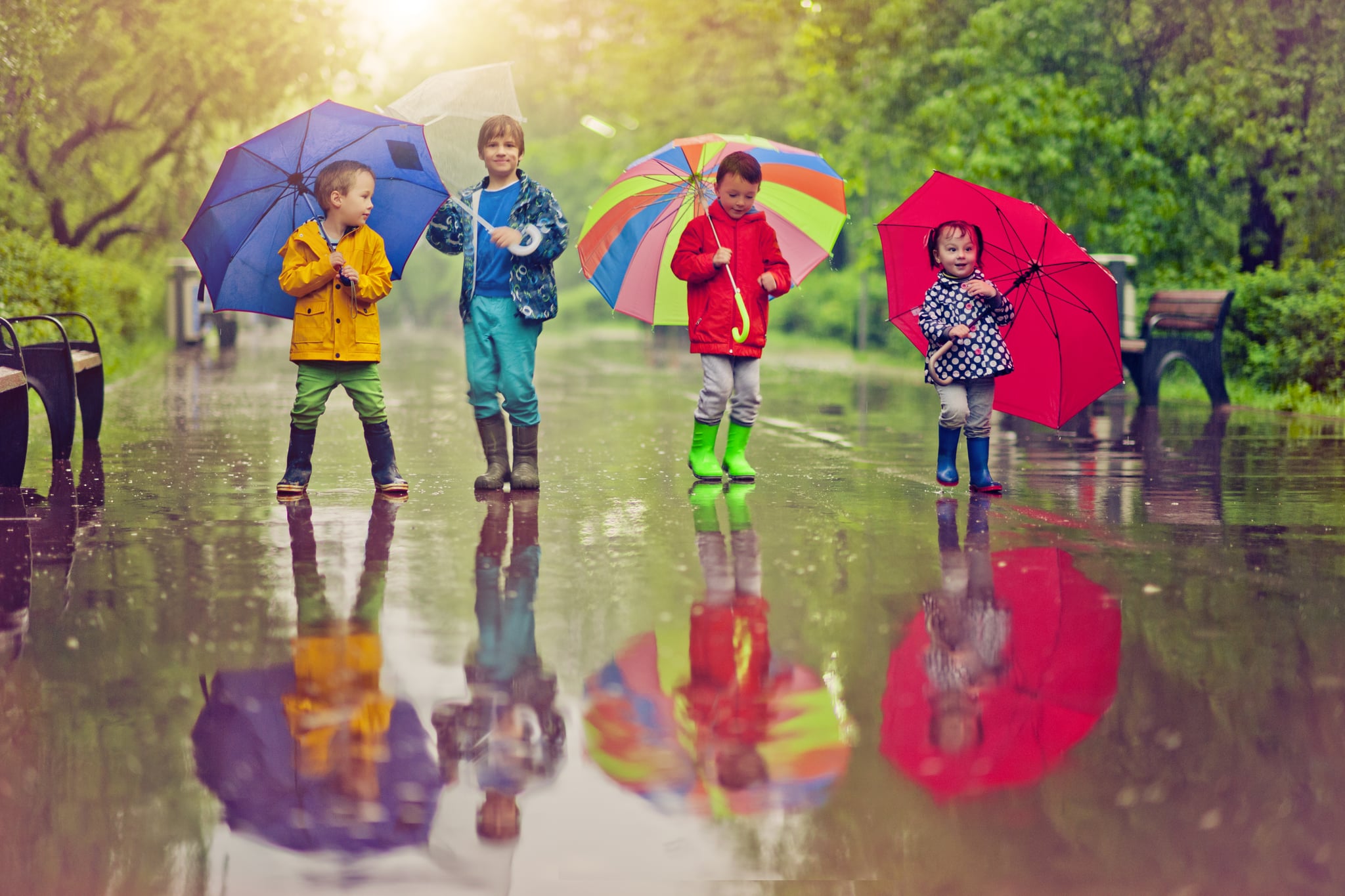 Little boys and girl happily walking under umbrella in park