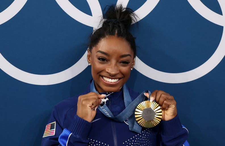 PARIS, FRANCE - AUGUST 01: (EDITOR'S NOTE: Alternate crop) Gold medalist Simone Biles of Team United States poses with the Olympic Rings and a goat charm on her necklace during the Artistic Gymnastics Women's All-Around Final medal ceremony on day six of 