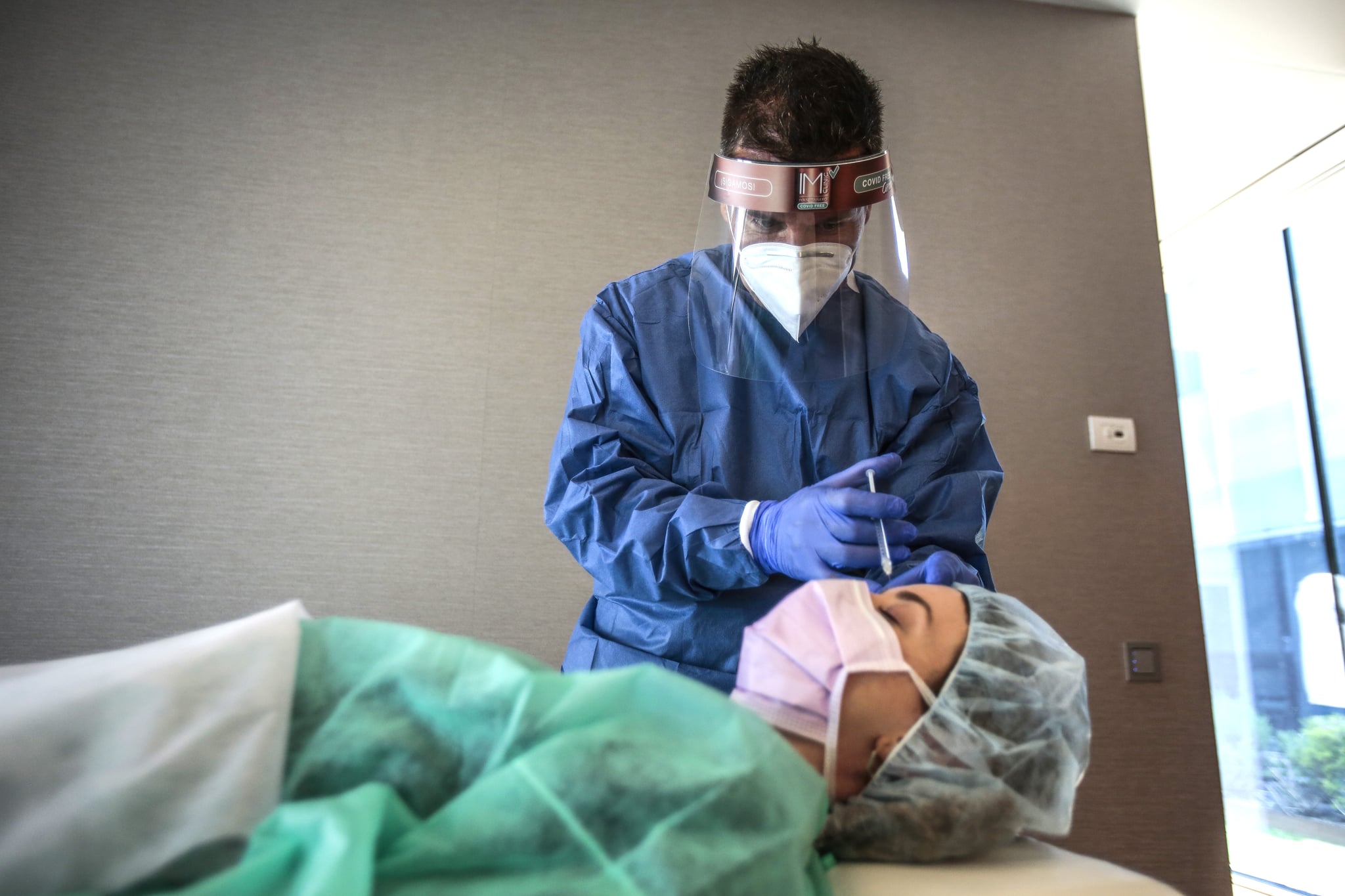 SANT CUGAT, SPAIN - MAY 11: Dr. Ivan Manero injects a botox treatment to Cristina wearing PPE kit as a part of the new protocols for action and protection against the Covid 19 pandemic during the demonstration for the photographer at IM Ivan Manero Aesthetic Surgery Clinic  on May 11, 2020 in Sant Cugat, Spain. Some parts of Spain have entered the so-called 