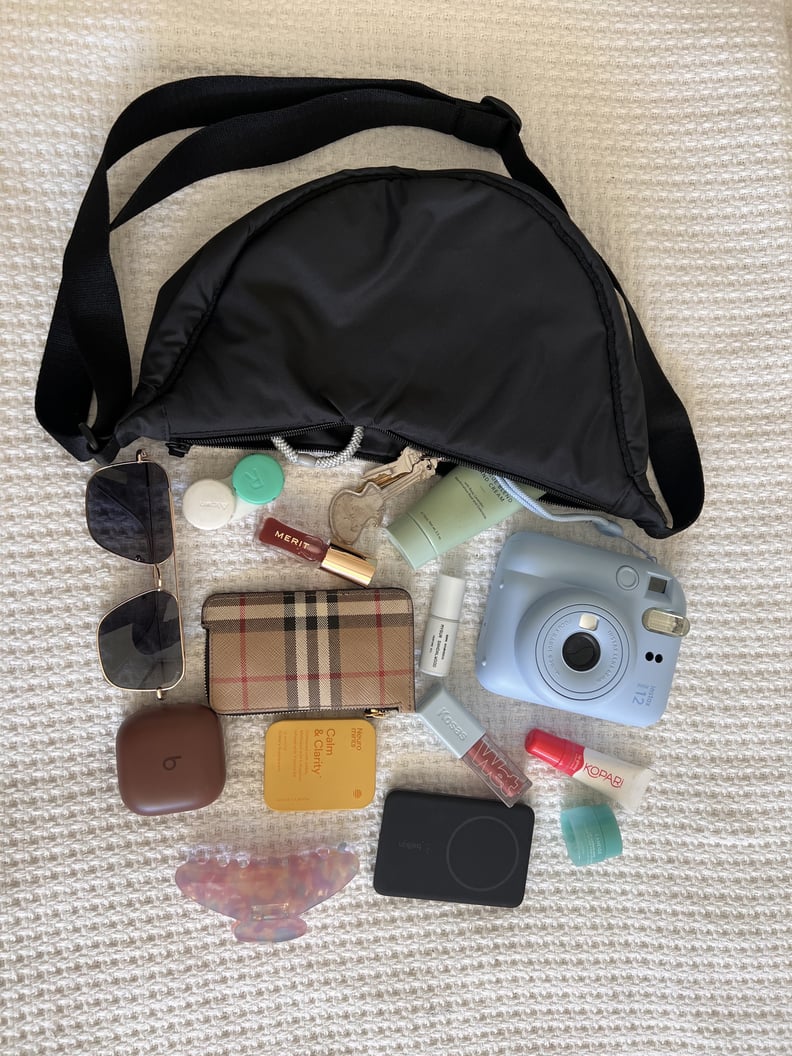 The Uniqlo Round Mini Shoulder Bag in black with phone, wallet, keys, earbuds, portable battery pack, claw clip, contacts lens case, sunglasses, a rollerball perfume, lip products, hand lotion, mints, and Instax camera.