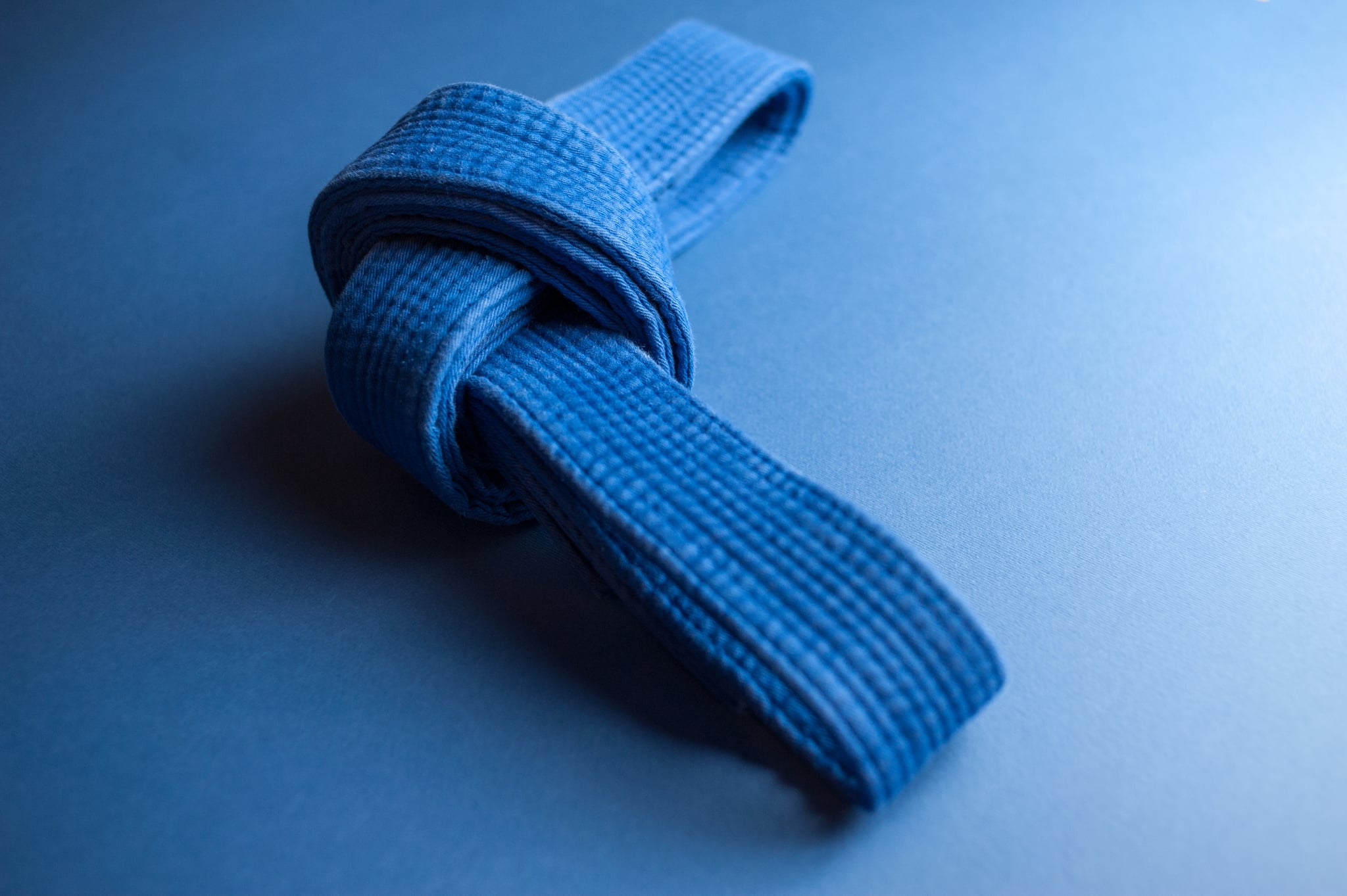 Blue judo belt tied in a knot isolated on blue background