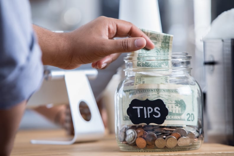Unrecognizable male coffee shop customer places cash into a tip jar.