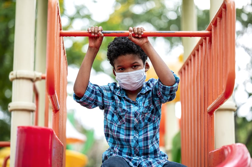 Lonely boy wearing protective face mask while playing at playground.