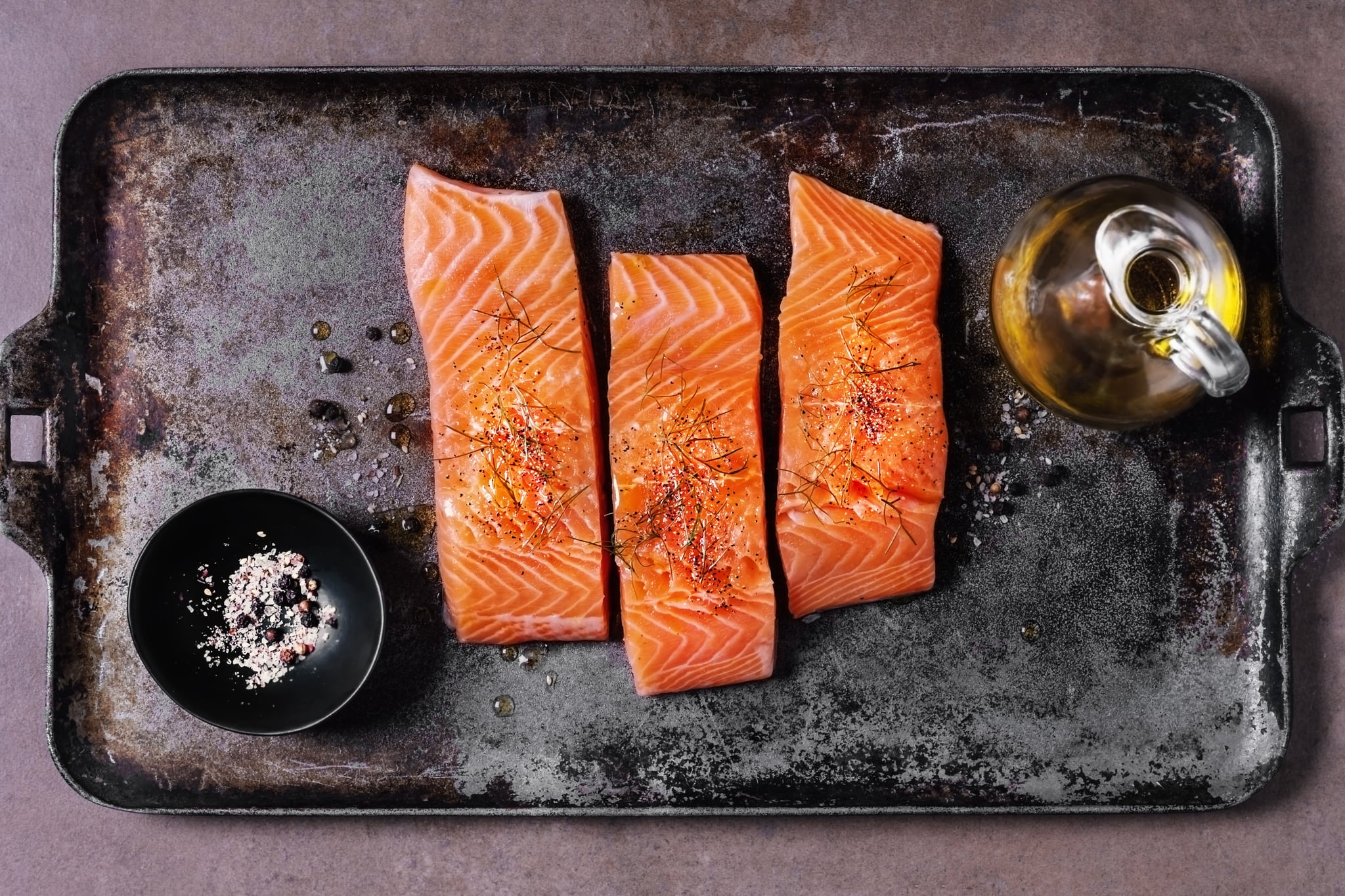 Slices of fresh salmon with spices and olive oil on a metal tray