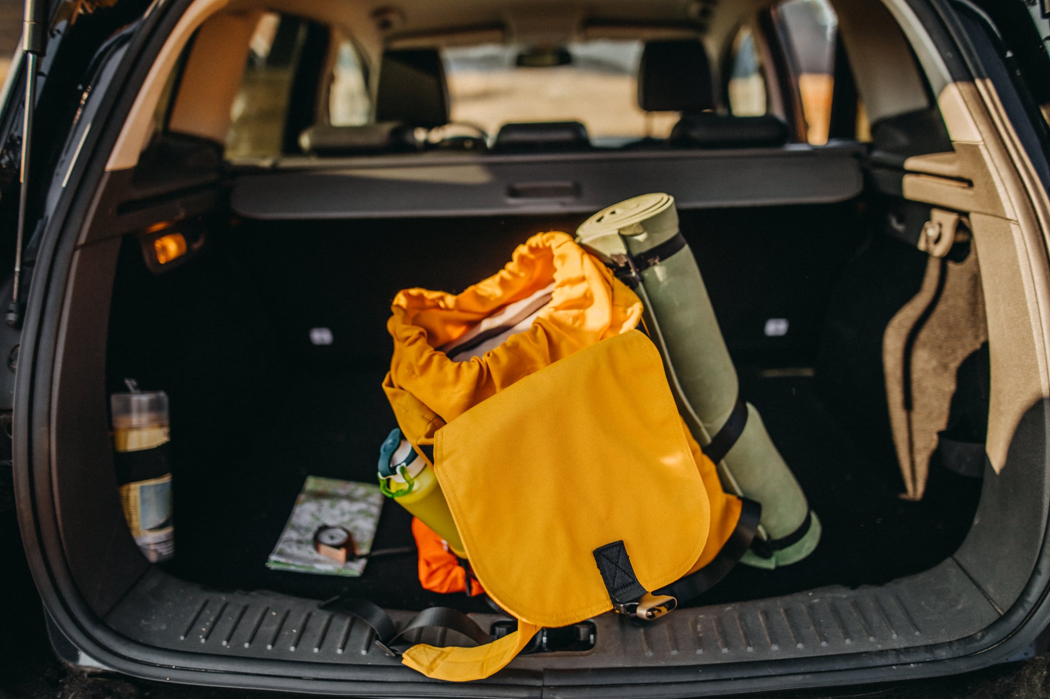 an open car trunk with car camping essentials like a backpack and sleeping pad