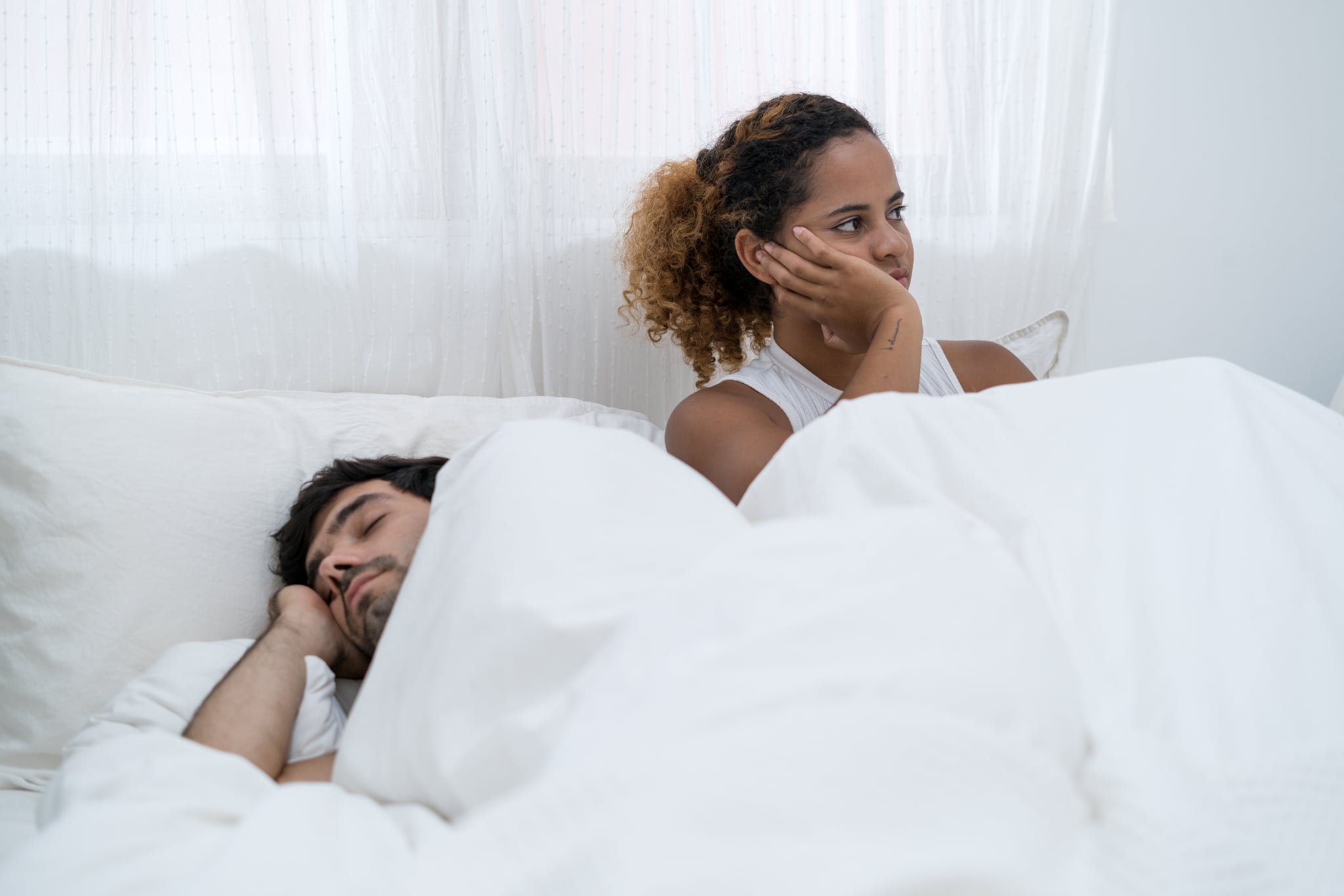 Frustrated girlfriend sad in bed while boyfriend ignoring his girlfriend on bed.