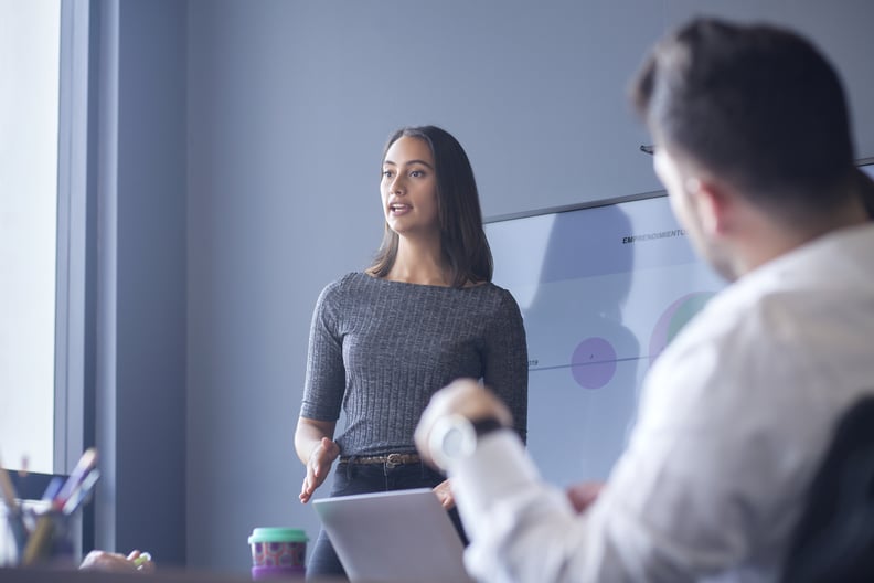Woman of Latin ethnicity between 25-35 years is at work conducting a conference for her co-workers in the boardroom