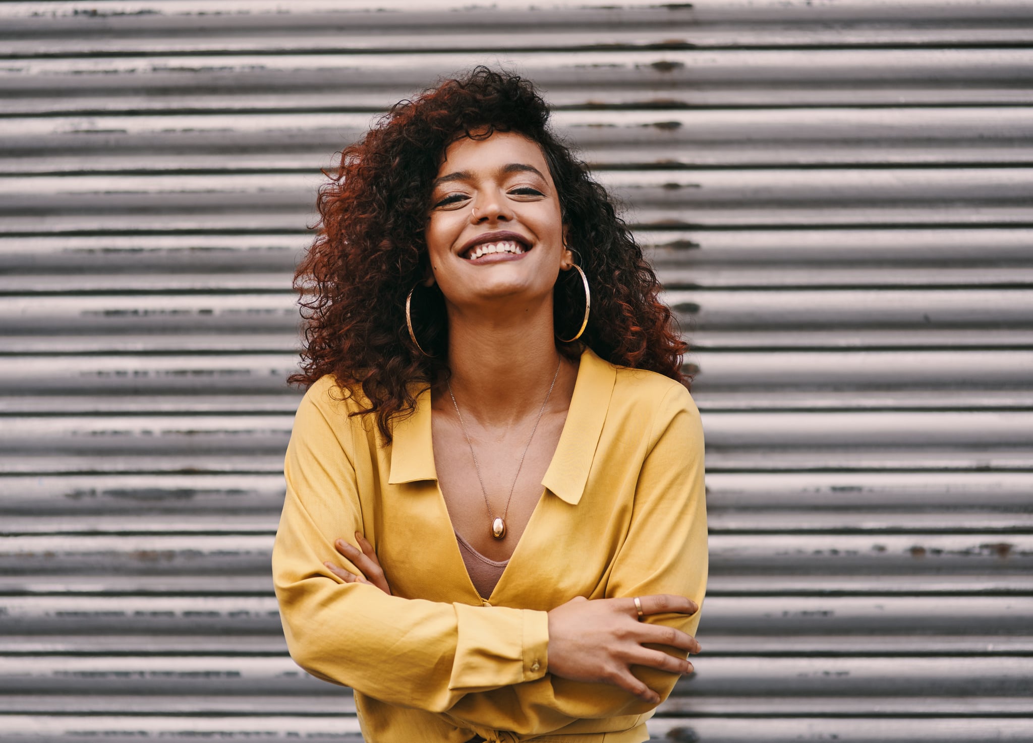 Cropped portrait of an attractive young woman smiling while standing with her arms folded against an urban background