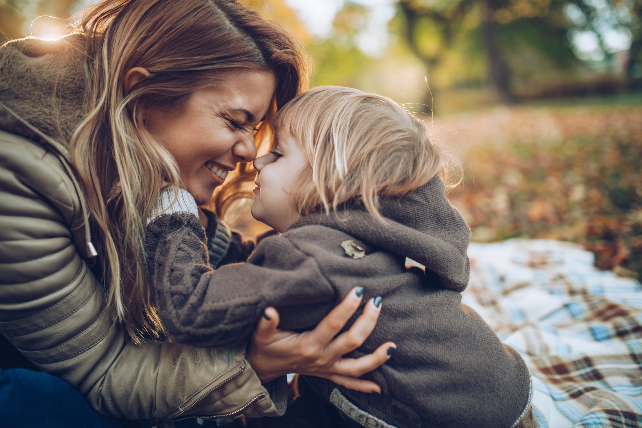 Happy mother and her small son having fun while touching with noses in autumn day.