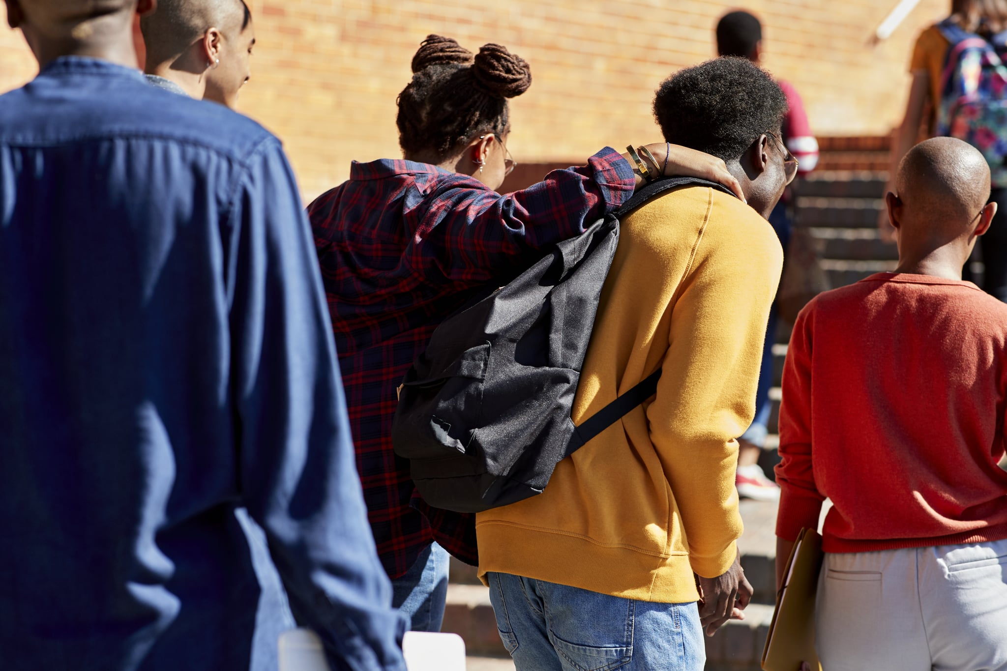 后视图男人和女人走的手搭在肩膀上和朋友在大学校园在阳光灿烂的日子
