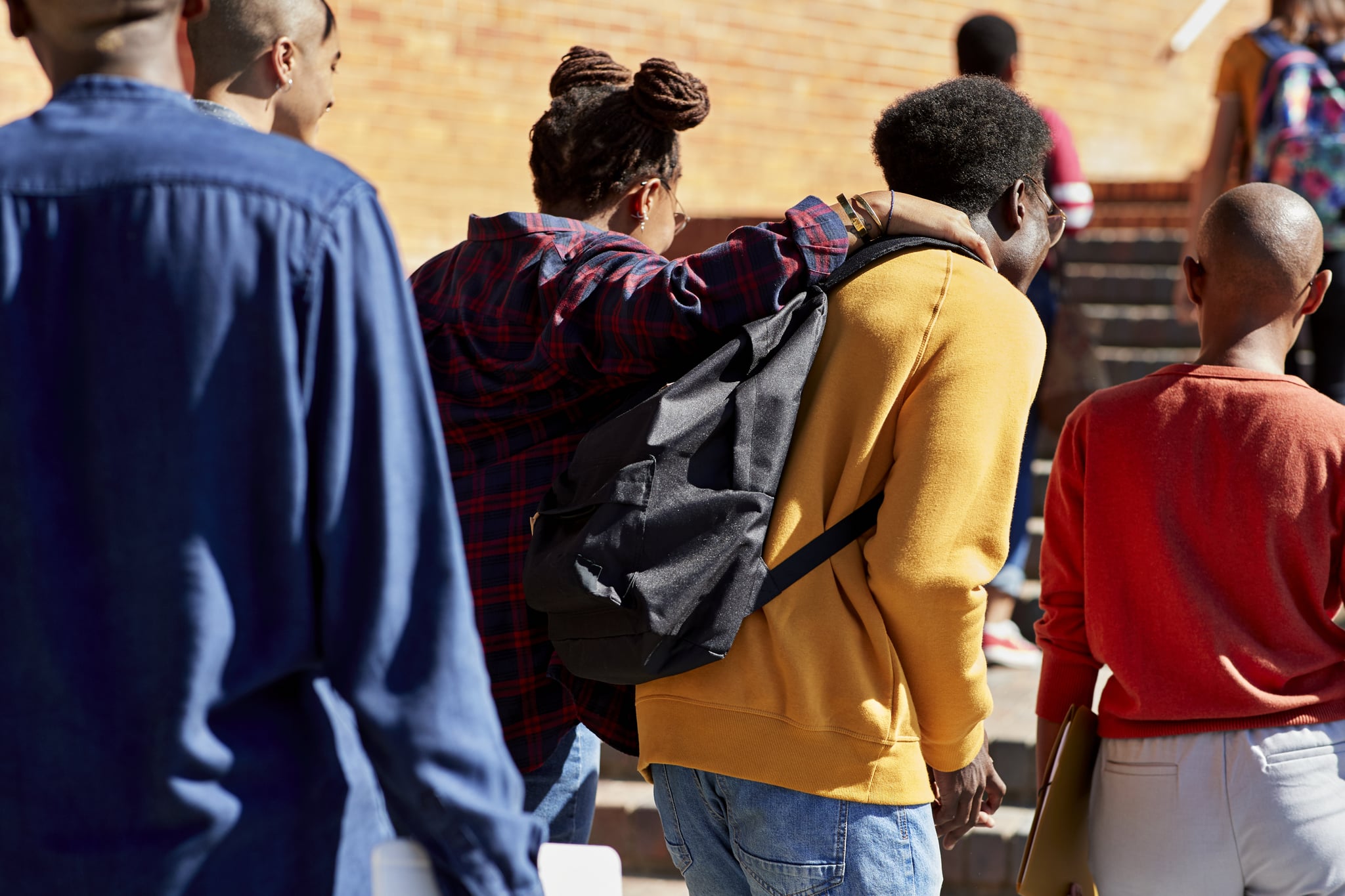 Rear view of man and woman walking with hand on shoulder with friends at university campus during sunny day