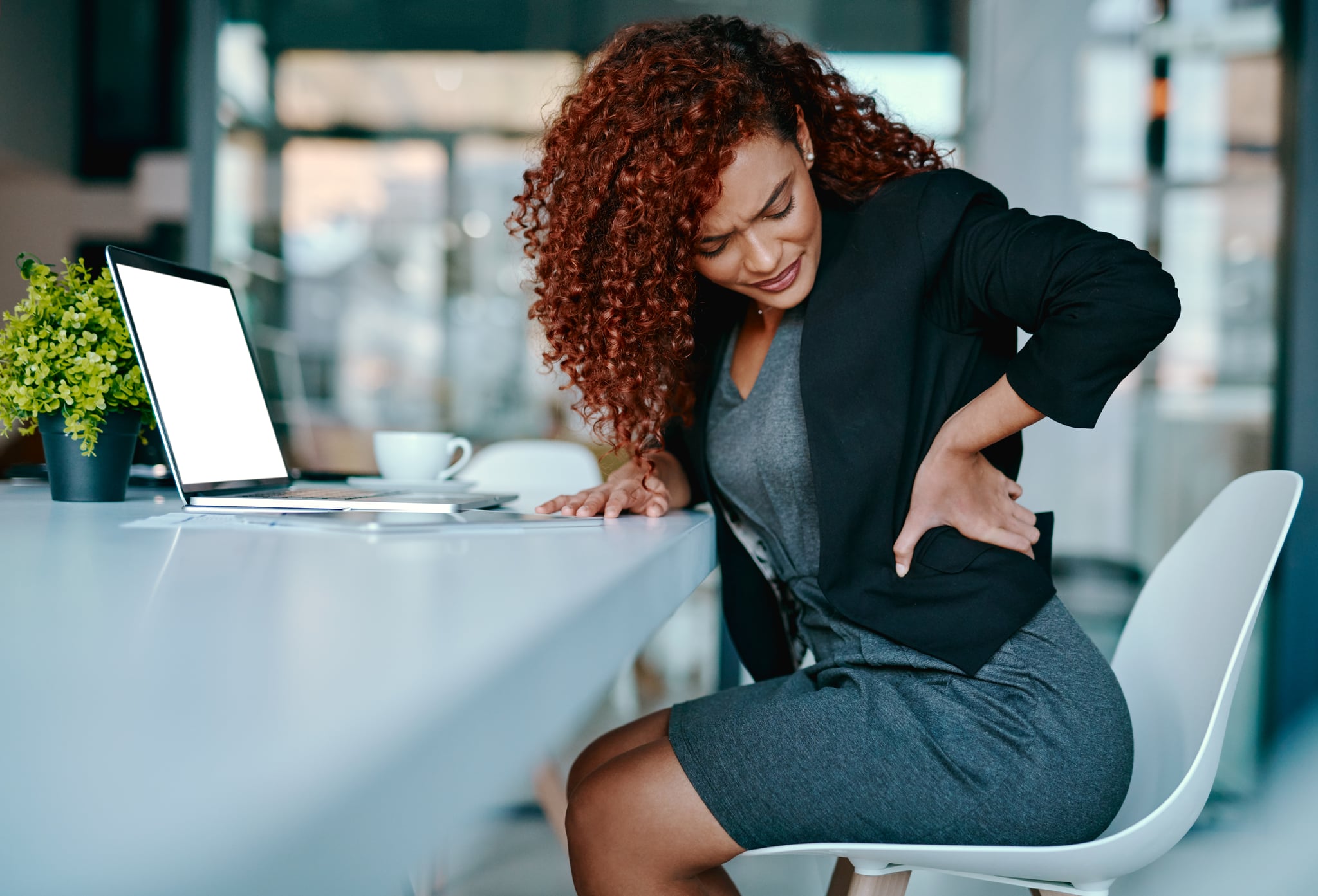 Shot of a young businesswoman suffering with back pain while working in an office