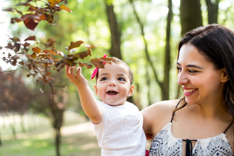 A joyful latin mother carrying her baby daughter and smiling in a horizontal waist up shot outdoors.