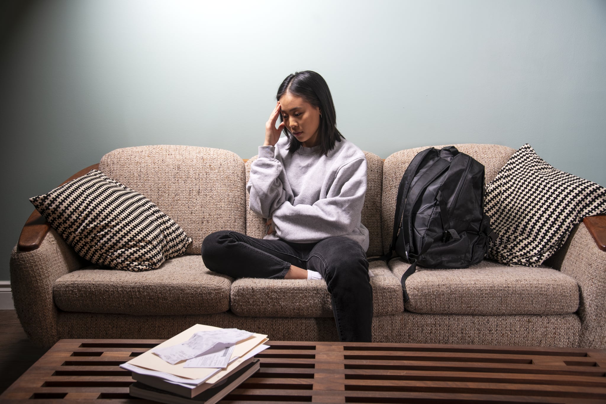 A university student of Asian heritage experiencing financial or emotional stress at home in her apartment.