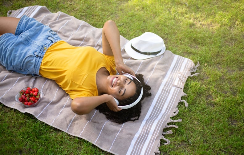 Above view of beautiful African American woman with headphones listening to music during picnic at park