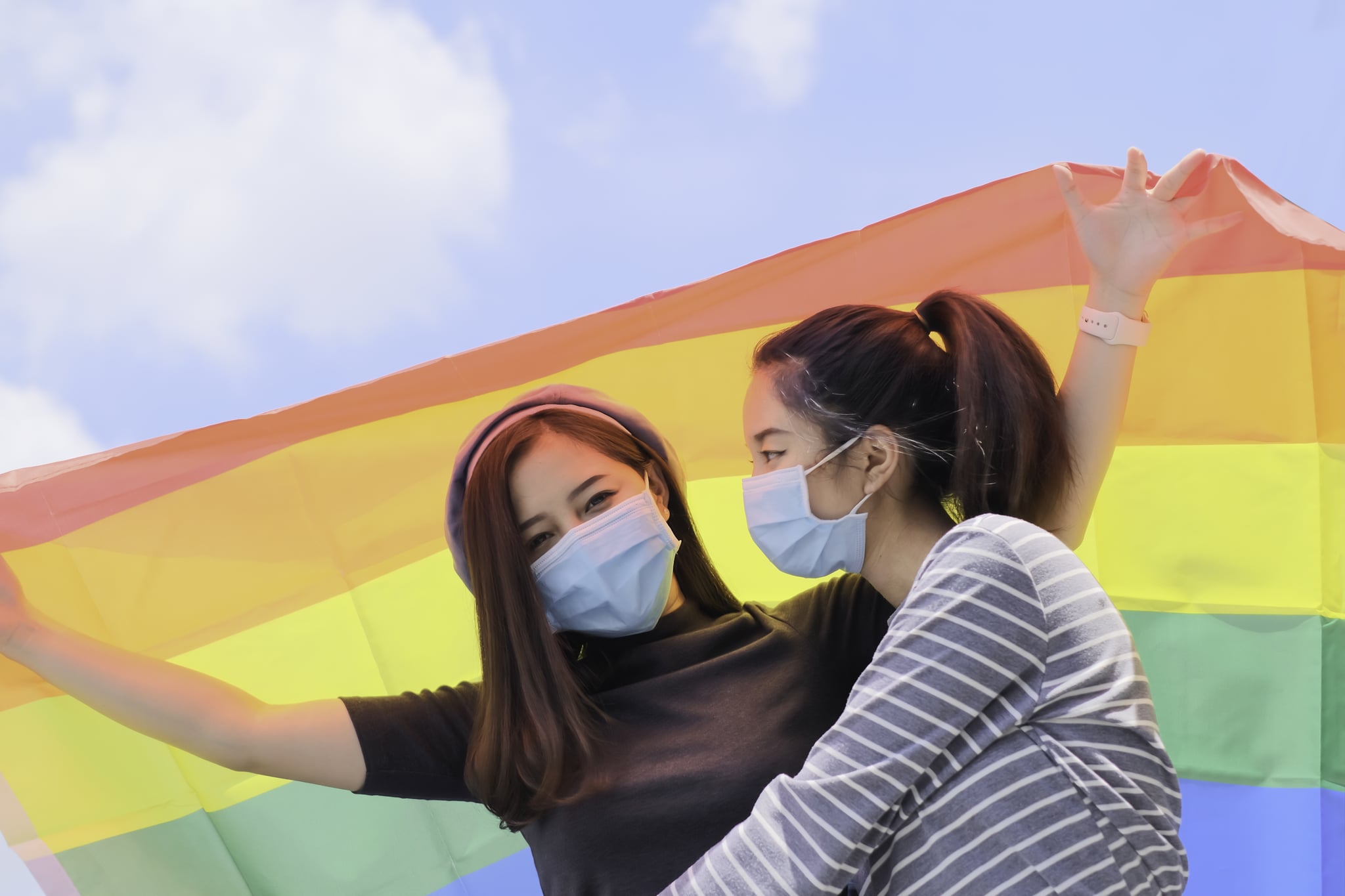 Two pretty Asian women LGTB wearing hyginic face mask and holding LGTB flag.