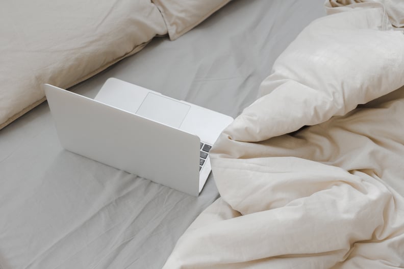 a laptop open on an unmade bed