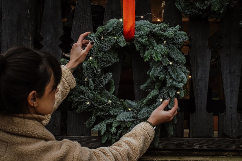 A natural setup outside a wooden house with evergreen pine Christmas wreaths and decoration crafts. Woman decorating home.Zero waste decorating, small business, florist work before holidays