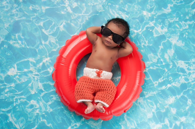 两个星期老新生儿男孩睡在一个小的充气游泳圈。他穿着钩针编织的董事会短裤和黑色太阳镜。