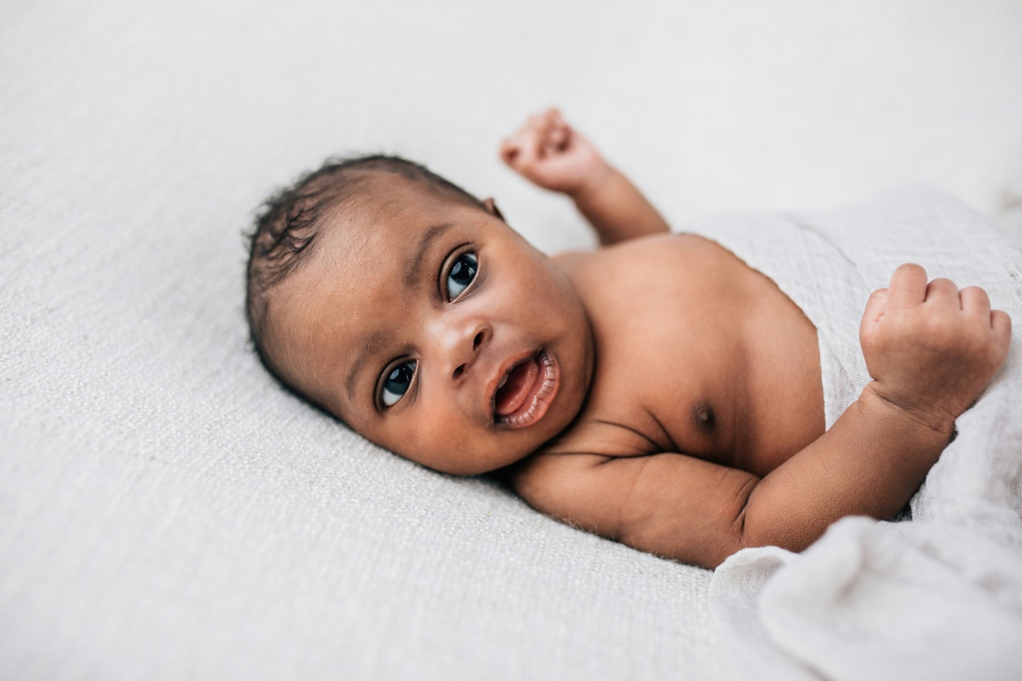 Happy, awake and cute African-American newborn baby boy laying on a cream-coloured blanket