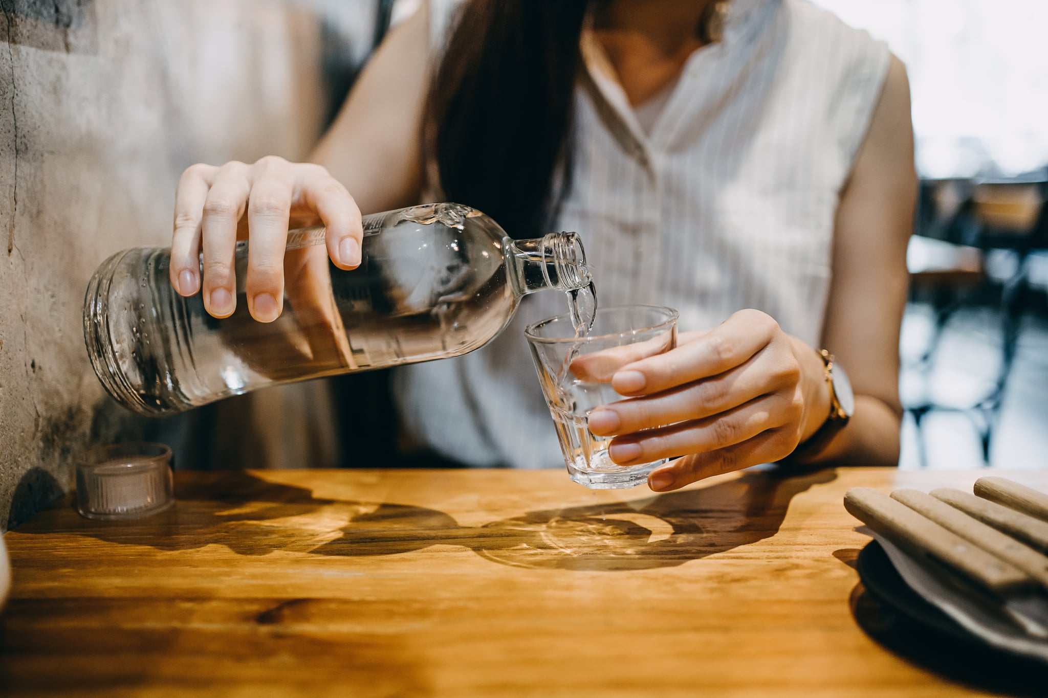 Midsection of young Asian woman pouring water from bottle into the glass in a restaurant