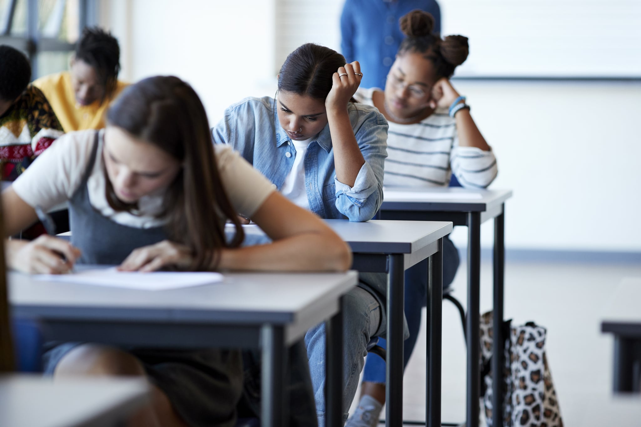 Young multi-ethnic female university students writing on papers at desks during exams in community college classroom