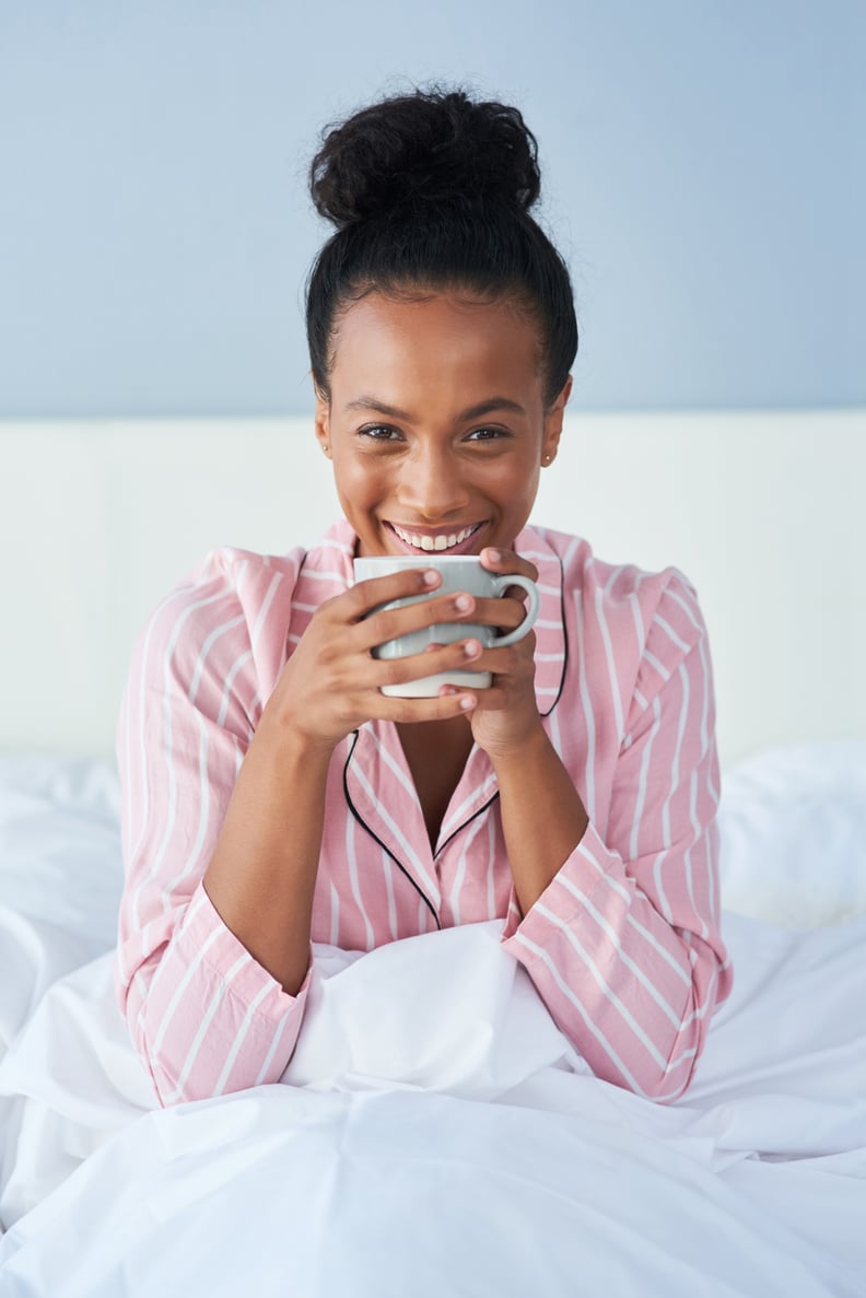 的一个有吸引力的年轻女人享受她早上咖啡在家躺在床上