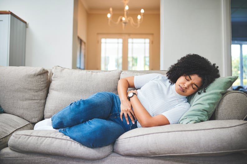 A Latina lies down on a couch and clutches her stomach.