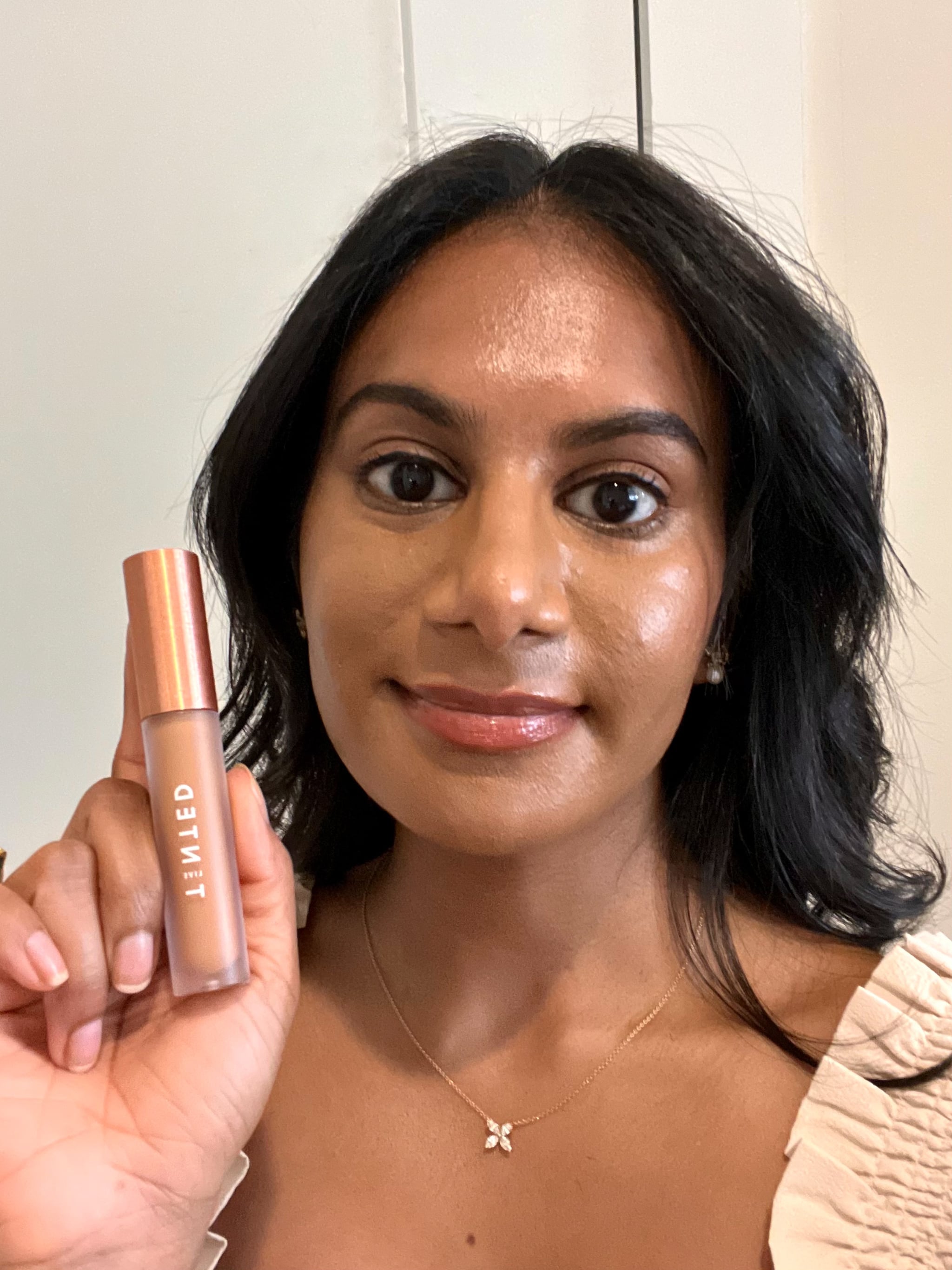 Woman wearing and holding the Live Tinted Hueskin Serum Concealer.