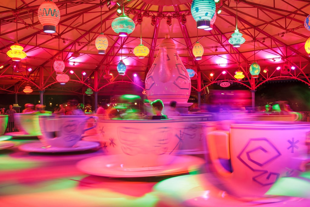 Teacups spin under coloured lights.