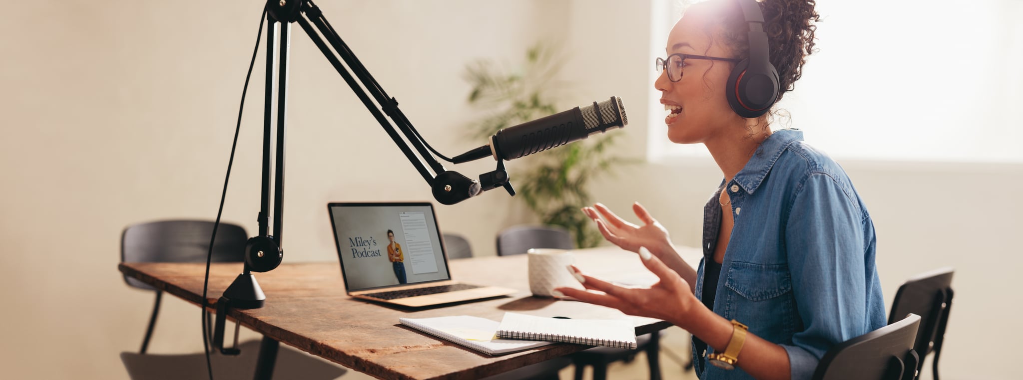 Female broadcasting her podcast from home. Woman wearing headphones talking into a microphone while working from home.