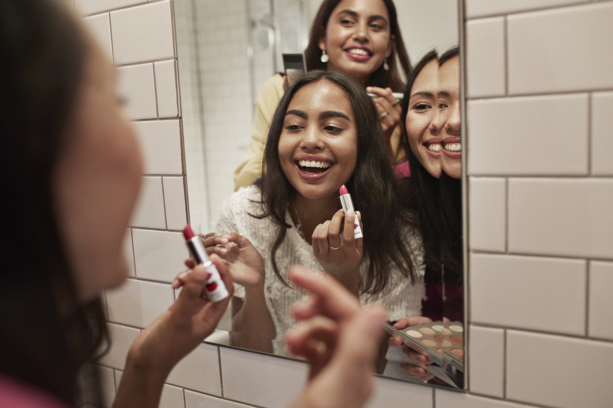 Smiling female friends applying lipstick while reflecting in mirror at home