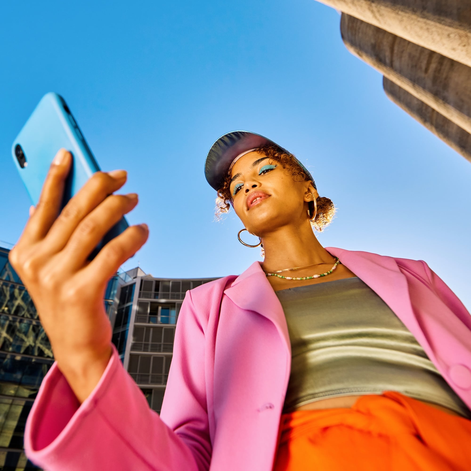 Young African American woman in colorful clothing using a smartphone. Low angle shot with concrete silos in the background. Urban fashion and technology concept.