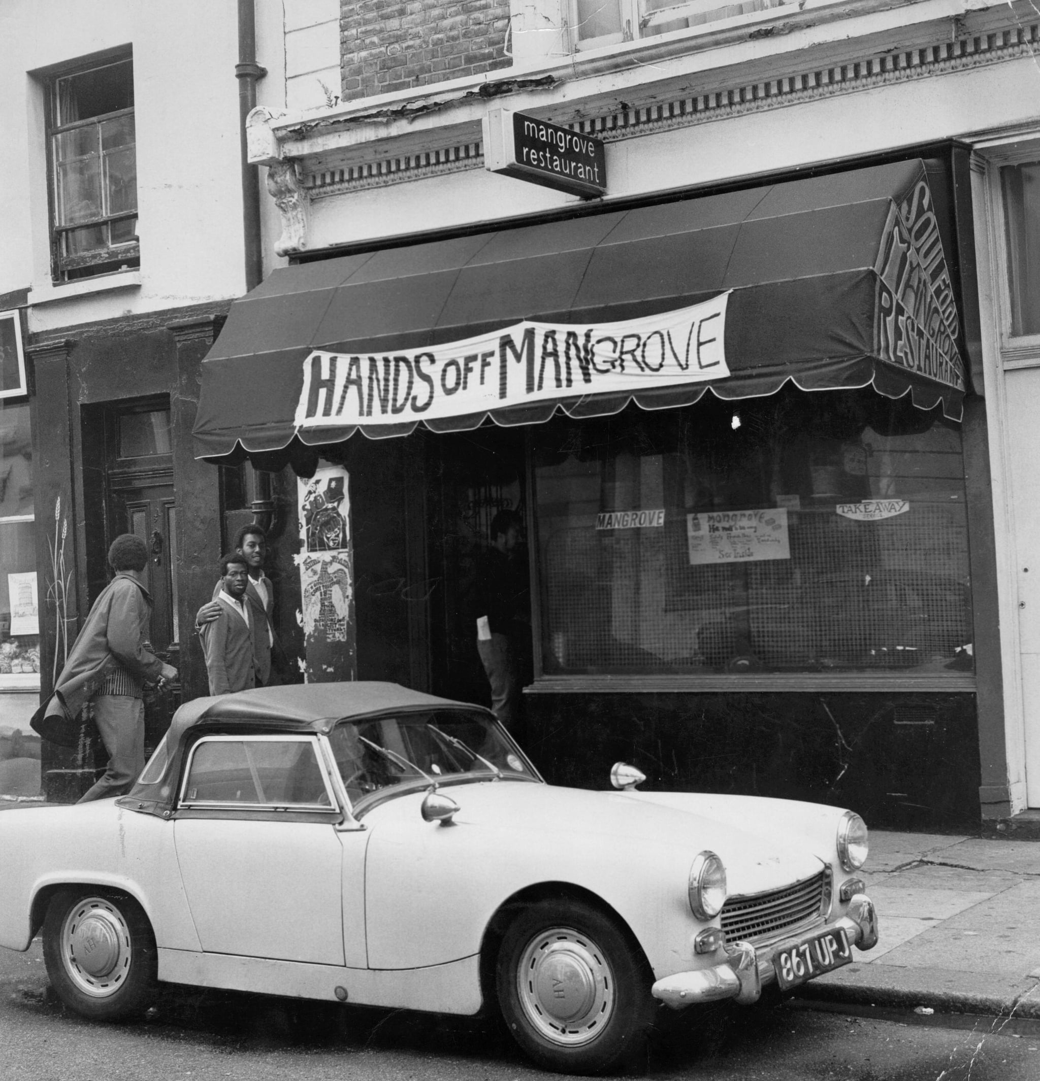 Four men entering the Mangrove, a Caribbean restaurant on All Saints Road, Notting Hill, London, 10th August 1970. The restaurant, seen here with a banner reading: 'Hands Off Mangrove' above it, has been repeatedly raided by the police in the last year, prompting a protest march to be organised by local residents. (Photo by Evening Standard/Hulton Archive/Getty images)