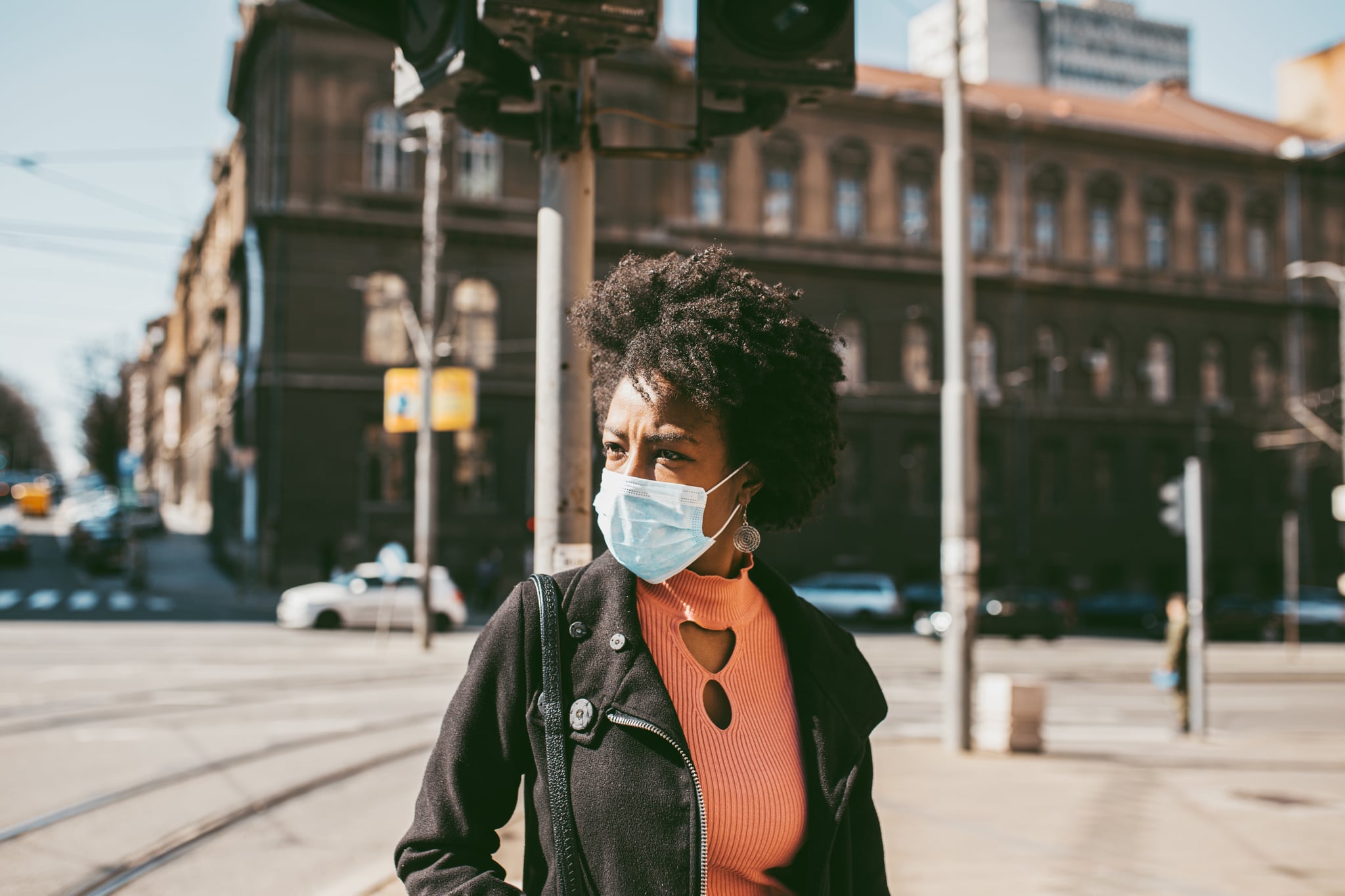 Young Afro American woman standing on city street with protective mask on her face. Virus pandemic and pollution concept.