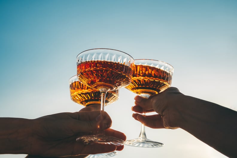 A close-up shot of friends clinking orange wine glasses at sunset.